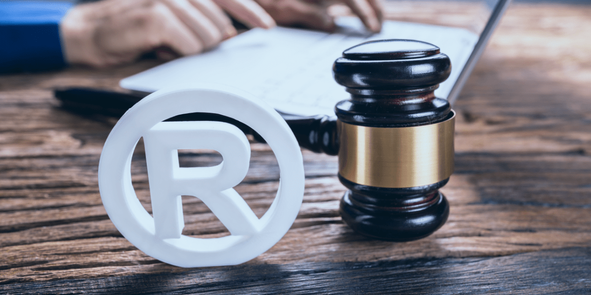 Person filling out a trademark application with the registered trademark symbol and a judge's gavel in the foreground.