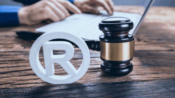 Person filling out a trademark application with the registered trademark symbol and a judge's gavel in the foreground.