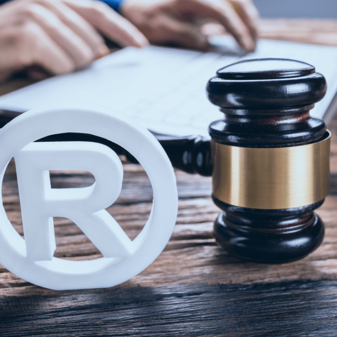 Person filling out a trademark application with the registered trademark symbol and a judge's gavel in the foreground.