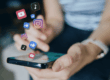 Person using a smartphone with social media app icons floating above, representing online sharing and copyright considerations for businesses.