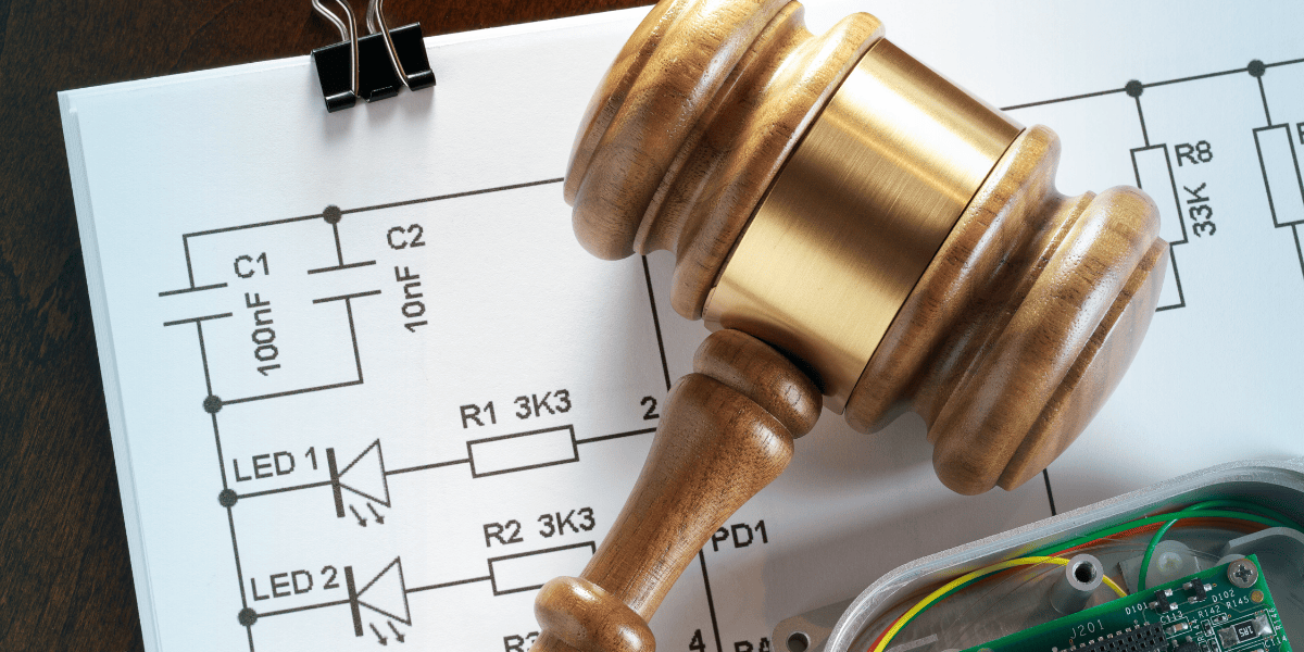 Wooden gavel resting on electronic circuit diagram and components, symbolizing patent law
