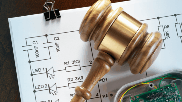 Wooden gavel resting on electronic circuit diagram and components, symbolizing patent law
