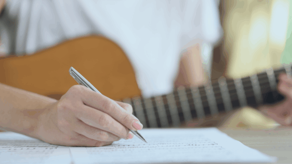 Musician writing in a notebook with a guitar in the background, illustrating the creation of original work.