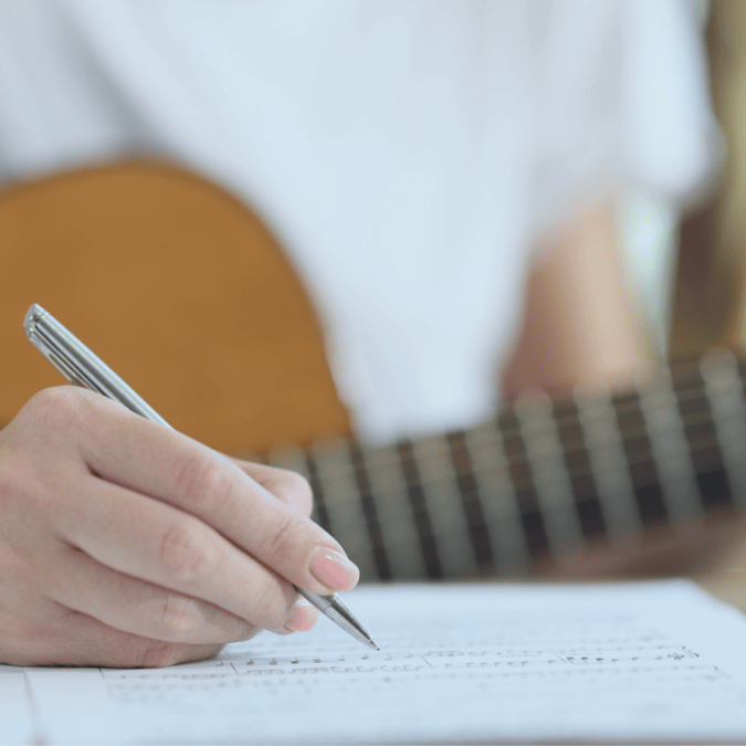 Musician writing in a notebook with a guitar in the background, illustrating the creation of original work.