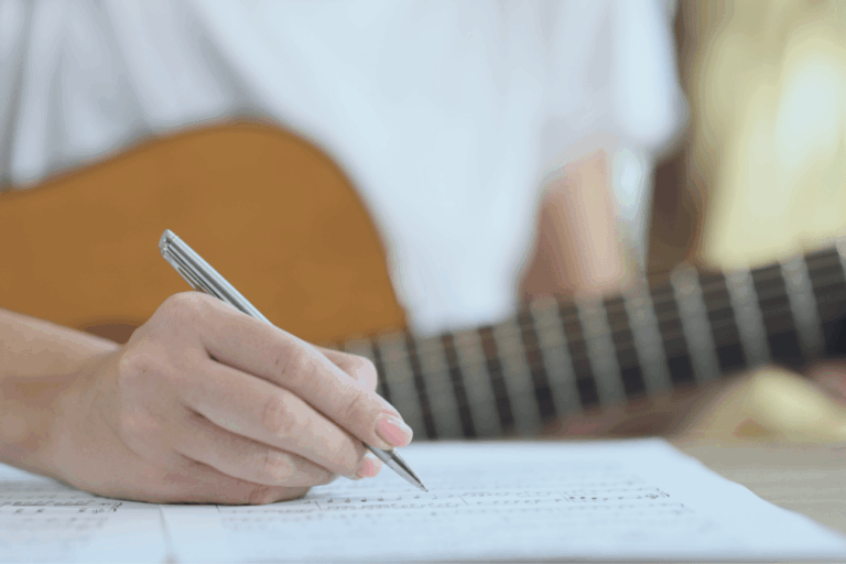 Musician writing in a notebook with a guitar in the background, illustrating the creation of original work.